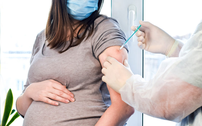 masked pregnant woman receiving a vaccine injection